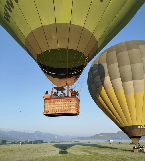 Une montgolfière avec des passagers à bord, une autre montgolfière en arrière-plan, et un paysage composé de montagnes et de champs. 4