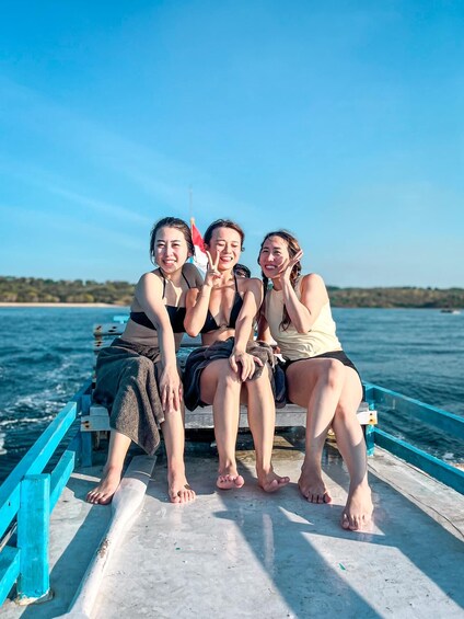 Four people sitting on a boat with a flag, on a body of water with a distant shoreline. 1