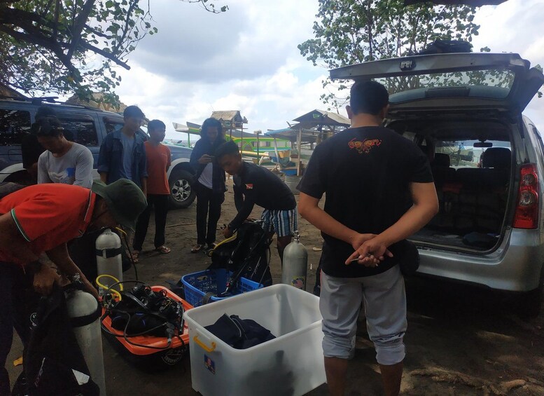 A group of people around a vehicle with a motorcycle and equipment in the trunk. 4
