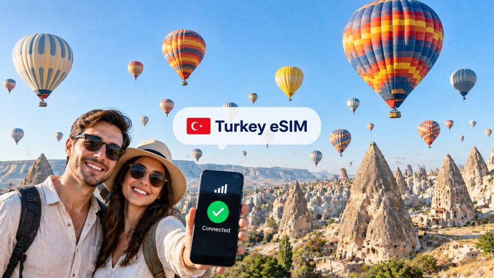 Una pareja con un teléfono inteligente que muestra un logo eSIM conectado, con globos aerostáticos y un paisaje de formaciones rocosas al fondo. 1