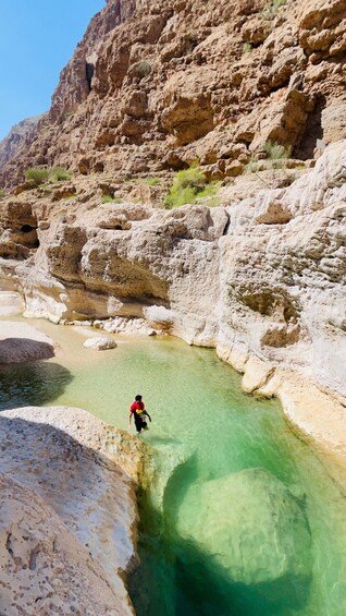 Une personne vêtue d’une chemise rouge traverse un plan d’eau peu profond et limpide, entouré d’un paysage rocheux. 4