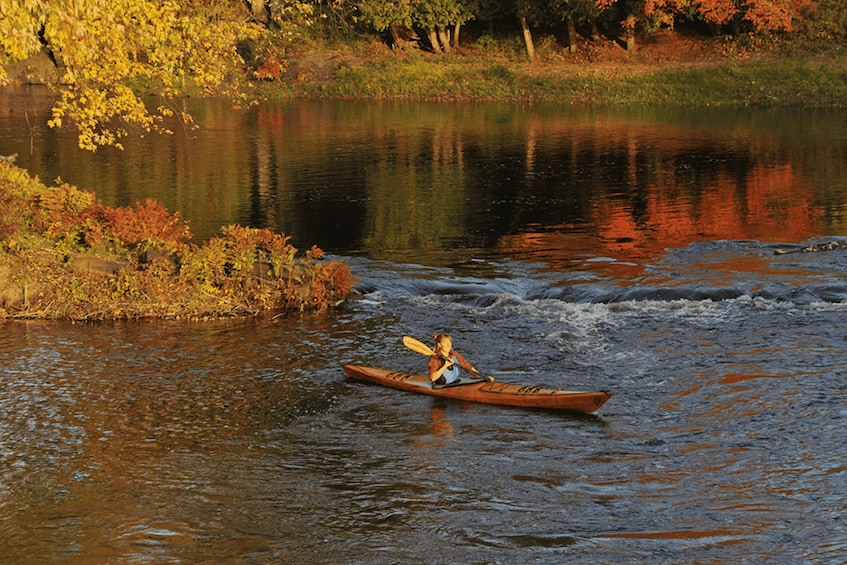 A person kayaking on a river surrounded by autumn foliage. 3