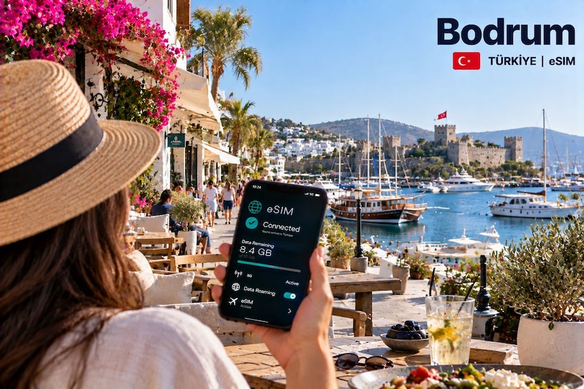 A person using a smartphone with eSIM data remaining, overlooking a harbor with boats and a castle in the background. 5