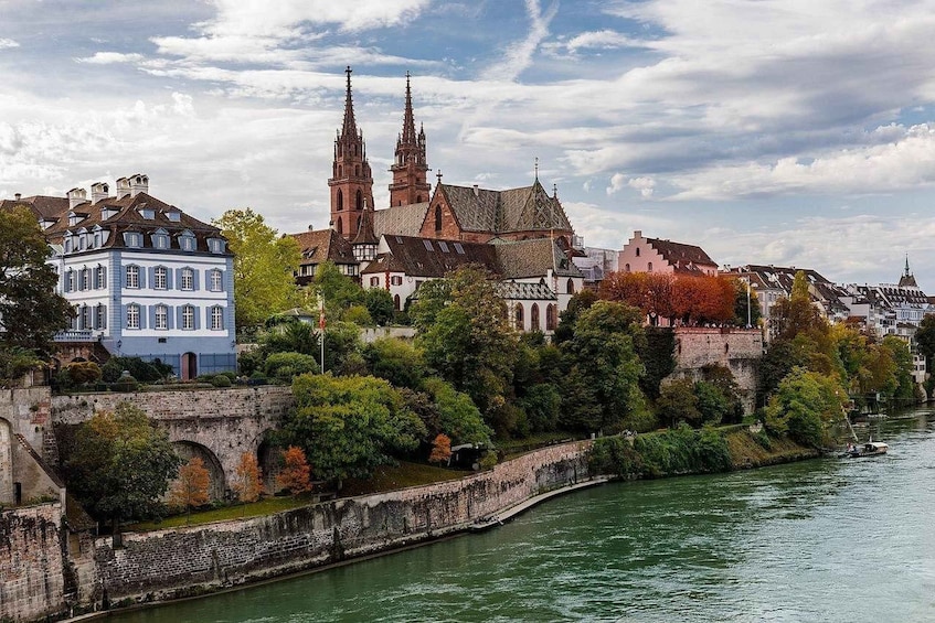 Eine historische Stadtansicht mit einer markanten Kirche mit zwei Türmen, einem Fluss und einer Mischung aus traditioneller und moderner Architektur. 1