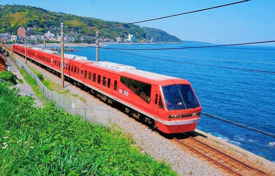 Un tren rojo sobre vías, cerca de una masa de agua con un paisaje montañoso al fondo. 1