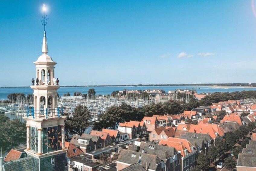 A coastal town with a prominent clock tower, red-roofed buildings, and a marina filled with boats. 3