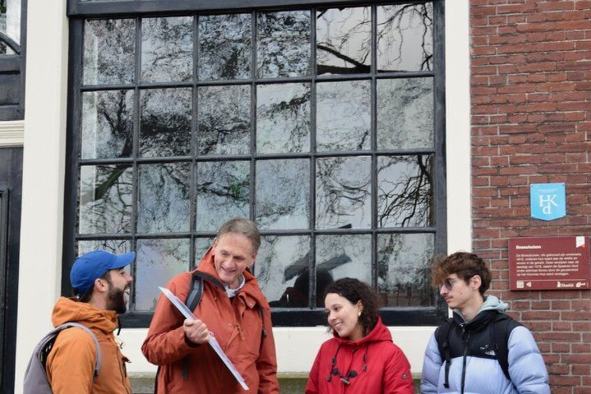 Four people standing in front of a building with a large window and a brick wall. 2