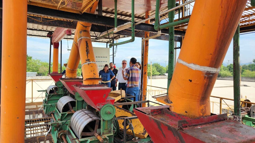 Industrial machinery with large orange and green pipes, a red funnel, and a group of people observing the equipment. 2