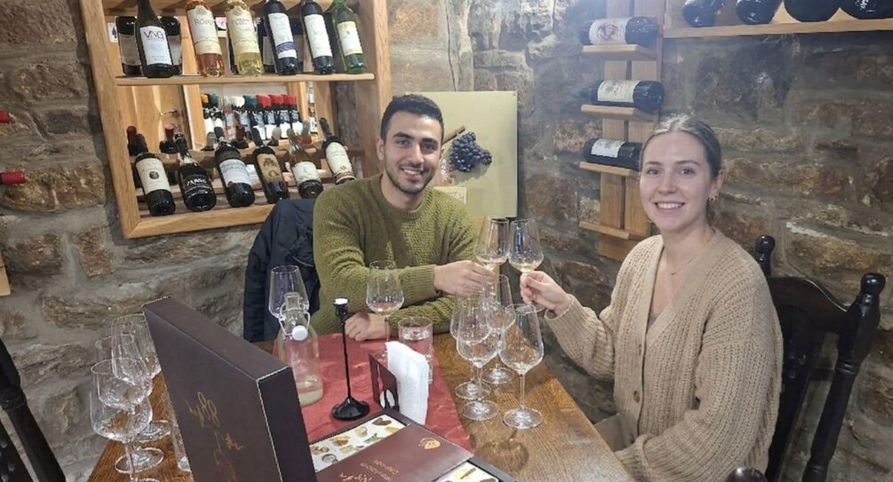 A person holding a wine glass at a table with several empty wine glasses and a wine bottle. 1