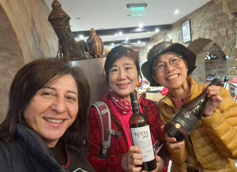 Three people holding bottles of wine in a stone-walled interior. 4