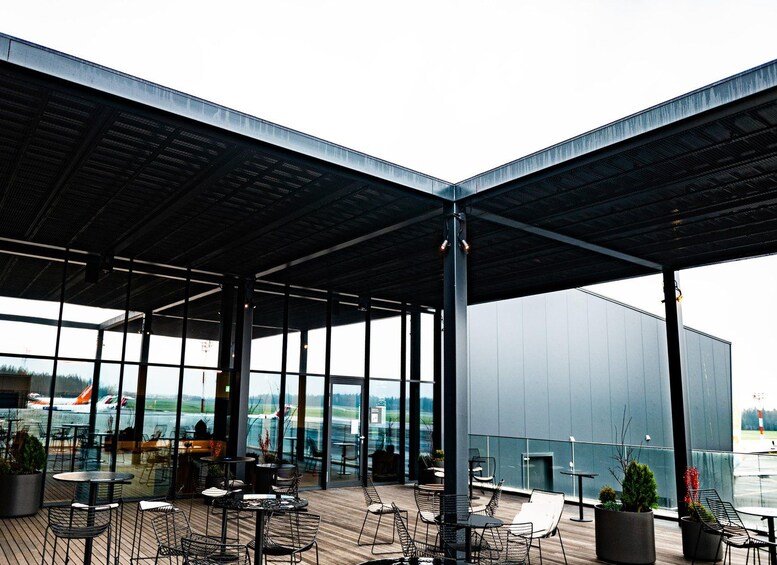 An outdoor seating area with tables and chairs, overlooking a body of water and airport. 1