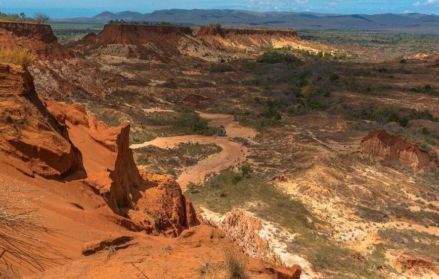 A rugged landscape with red rock formations, a winding river, and sparse vegetation. 2