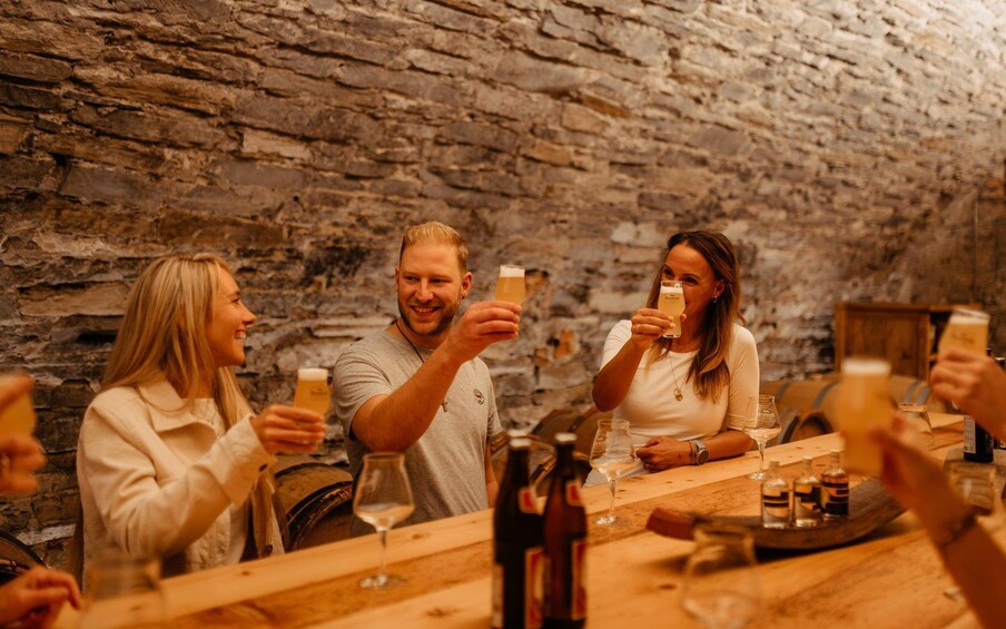 En grupp människor skålar med drycker vid ett rustikt träbord i ett rum med stenmurar. 2
