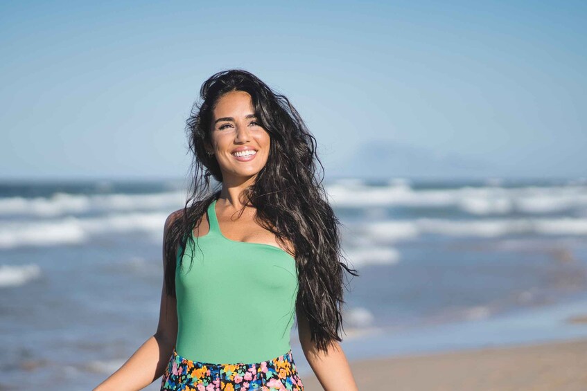 En person som står på en strand med vågor i bakgrunden. 1