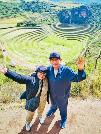 Two people standing on a dirt path with a terraced agricultural field in the background. 3