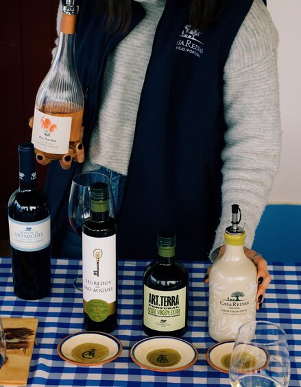 A table with various bottles of wine and olive oil, a person wearing a vest, and a checkered tablecloth. 3