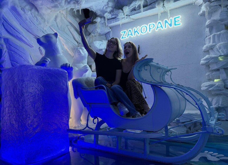 A person in a sled on an ice surface with a neon sign reading 'ZAKOPANE' in the background. 1