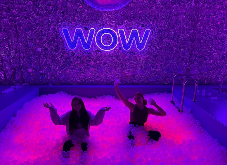 Two people in a ball pit with a neon 'WOW' sign in the background. 4