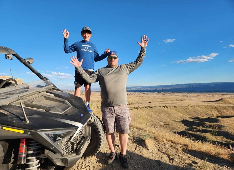 Two people standing next to a quad bike on a dry, open landscape with distant mountains. 4