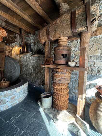 A rustic stone kitchen with a large stone mill, wooden beams, and a stone hearth. 4