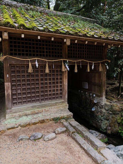 En traditionell japansk byggnad med ett mossbeklätt tak, fönster med trägaller och en repdekoration. 4