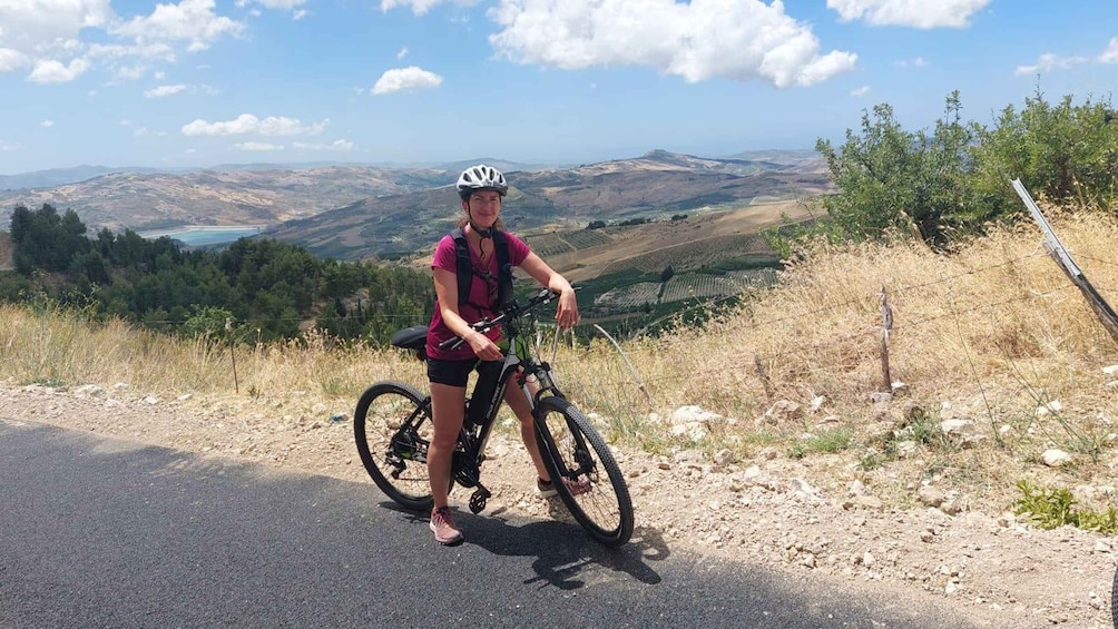 En person på en mountainbike som cyklar på en asfalterad väg med en vacker utsikt över kullar och en sjö i fjärran. 1