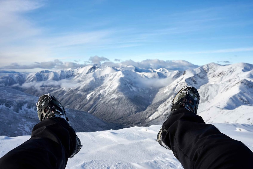 Une paire de pieds recouverts de neige, sur le sommet enneigé d’une montagne, sous un ciel dégagé. 1