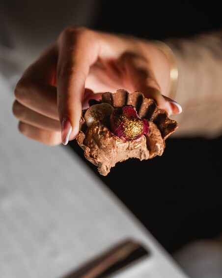 A hand holding a dessert with a golden decoration. 3