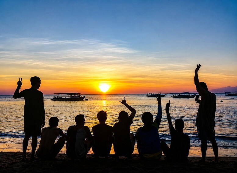 A group of people silhouetted against a sunset on a beach with boats in the water. 2