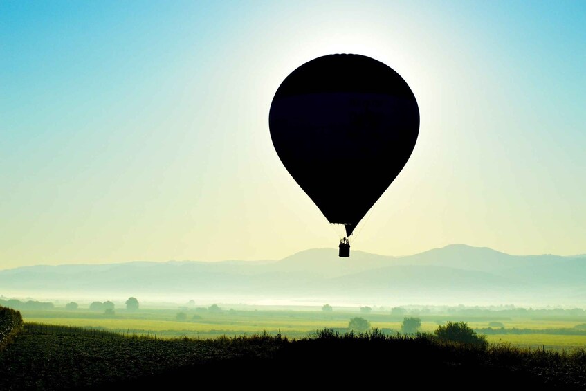 A hot air balloon over a landscape with fields and distant mountains. 5