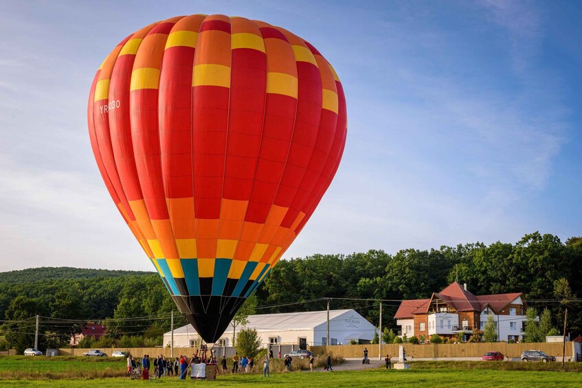 A hot air balloon with a colorful pattern, parked on a grassy field with buildings and trees in the background. 4
