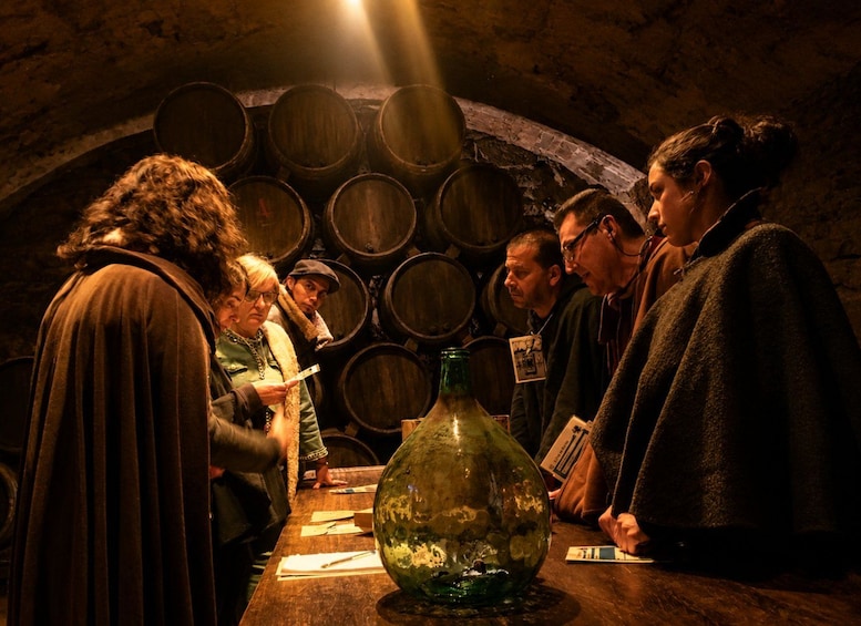Eine Gruppe von Menschen in einem Keller mit Holzfässern und einer großen grünen Flasche. 1