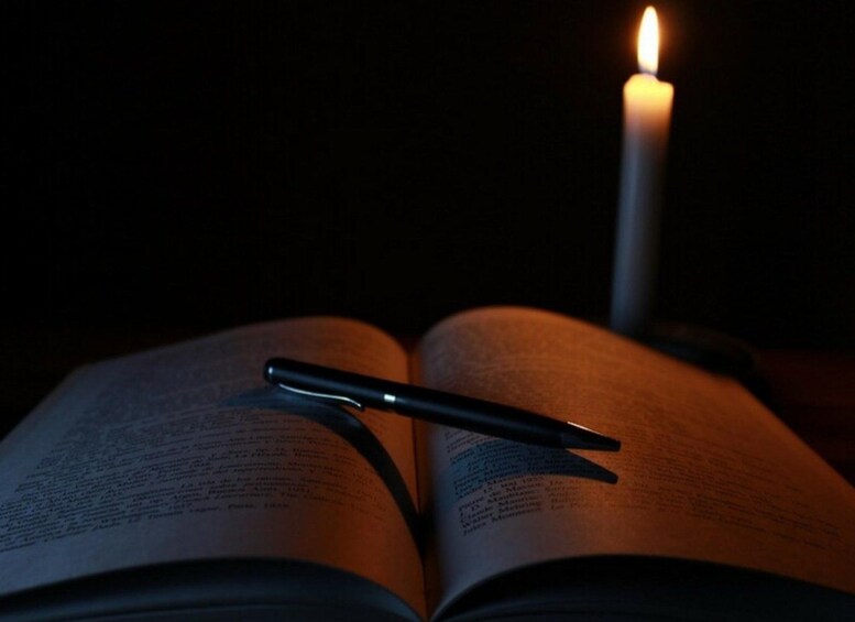 Ein offenes Buch mit einem Stift darauf und eine brennende Kerze im Hintergrund. 3