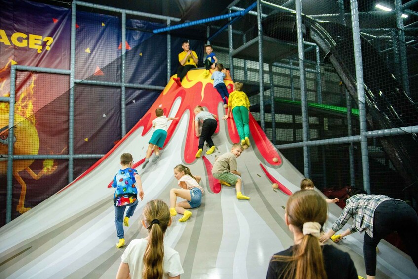 Children playing on a colorful indoor slide with safety netting around. 3