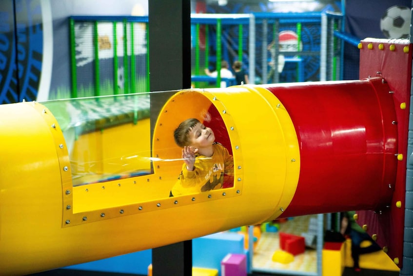 A child sliding down a yellow and red tube slide in an indoor play area. 5