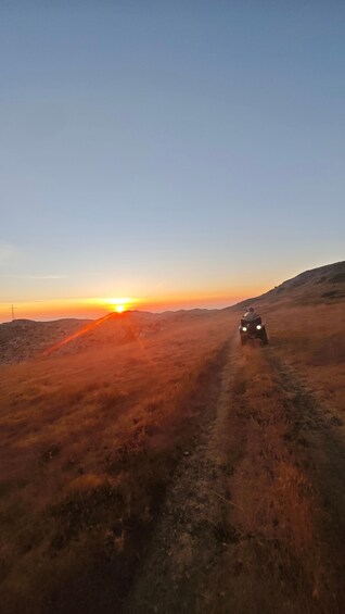 A dirt road leading towards a sunset with a vehicle in the distance. 3