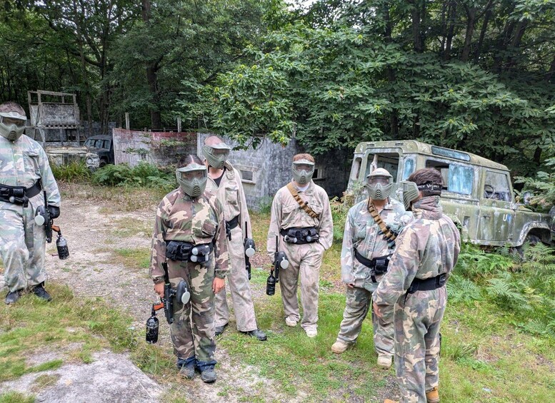 A group of people in military camouflage uniforms standing in a forested area with a vintage military vehicle in the background. 2