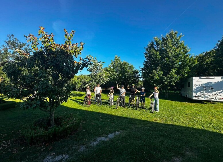 A group of people on bicycles in a grassy area with trees and a caravan. 1