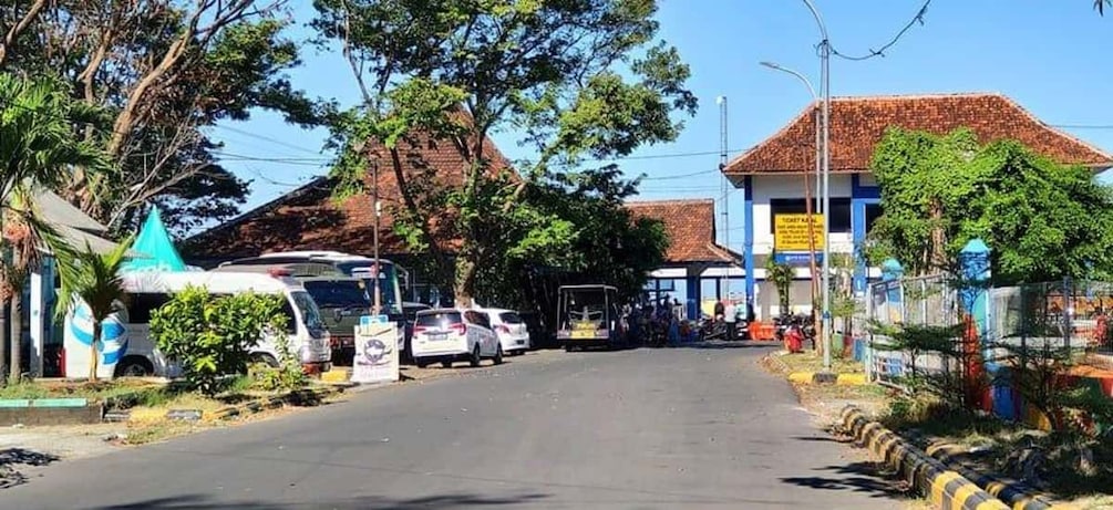 A street with parked cars, a bus, and a building with a blue and white facade. 5