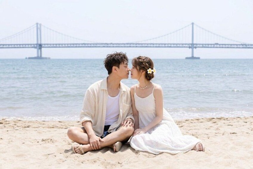 A couple sitting on a beach with a bridge in the background. 3