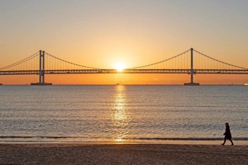 A bridge over water at sunset with a person walking on the beach. 2