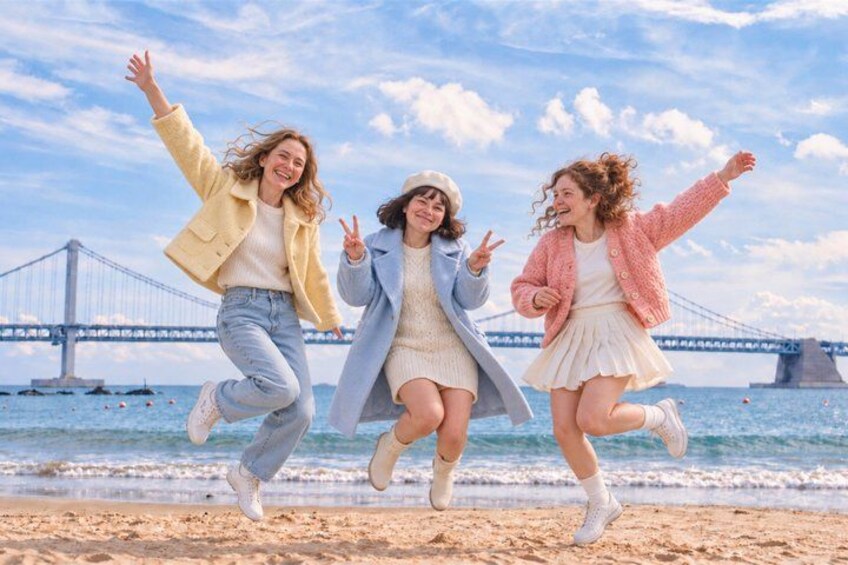 Three people jumping on a beach with a bridge in the background. 1