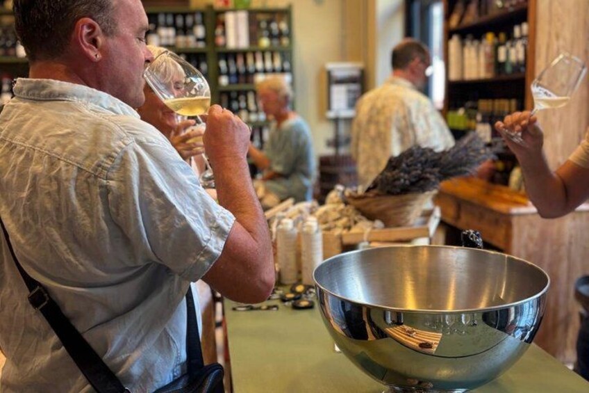 A person holding a glass of white wine, a metal bowl, and a wooden table in a bar setting. 1