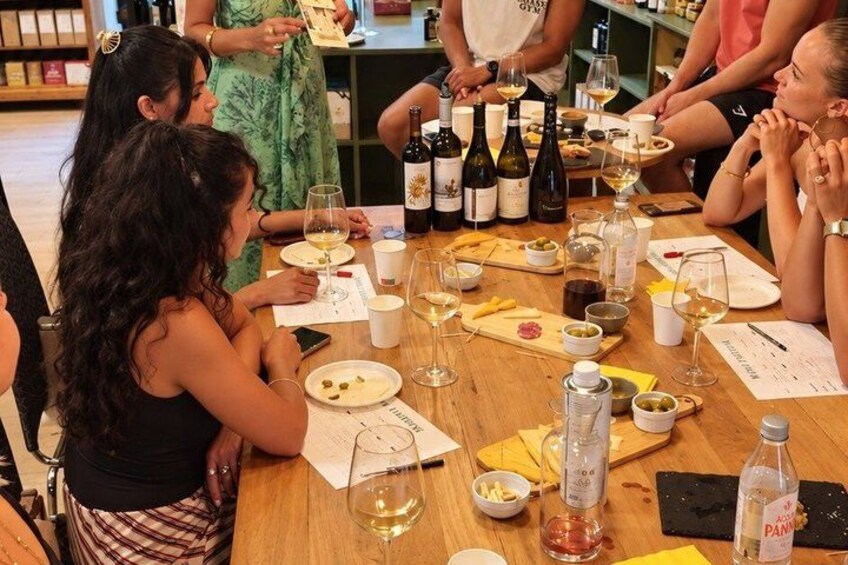 A group of people seated around a wooden table with wine bottles, glasses, and plates of food. 2