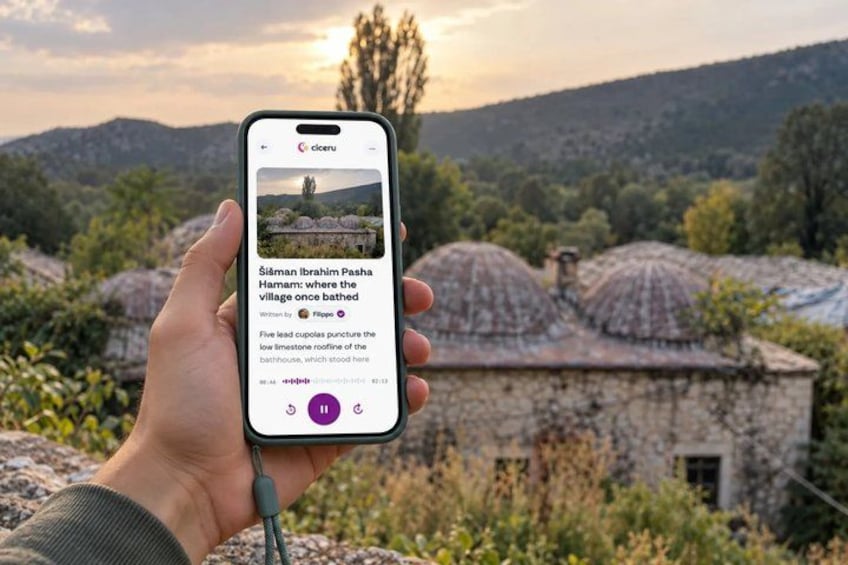 A hand holding a smartphone displaying a scenic view of a village with traditional houses and a mountainous landscape. 1