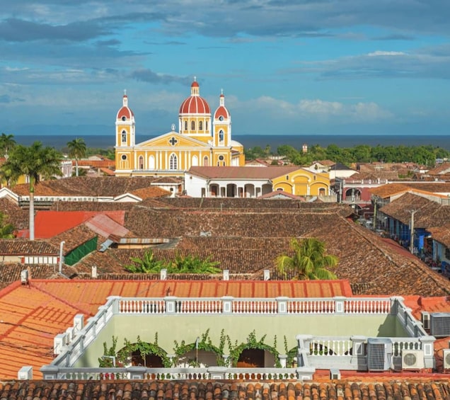 A historic cityscape with a prominent yellow cathedral with two domes, surrounded by colonial-style buildings and a coastal backdrop. 1