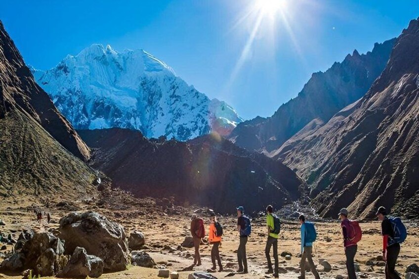 A group of people standing on a rocky mountain path with a snow-capped peak in the background. 5