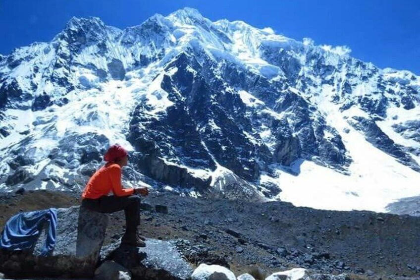 A person in an orange jacket sitting on a rock with a snow-covered mountain in the background. 1