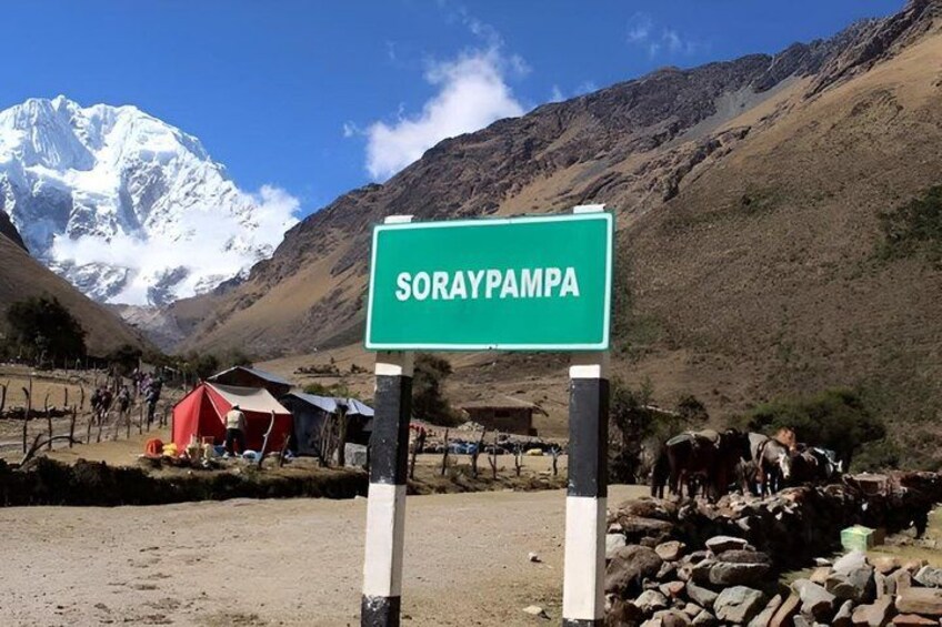 A sign reading 'SORAYPAMPA' with a mountainous backdrop and a small settlement with tents. 3