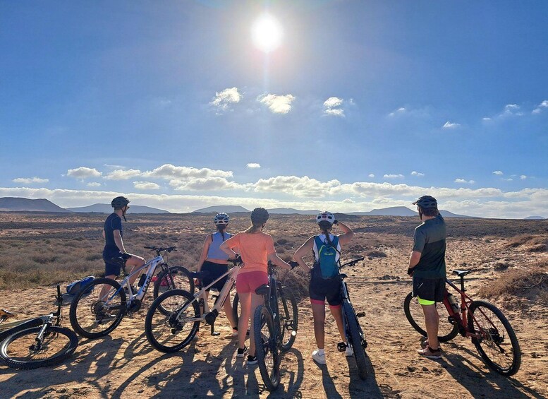 A group of cyclists on a dirt path with a desert landscape and mountains in the background. 1